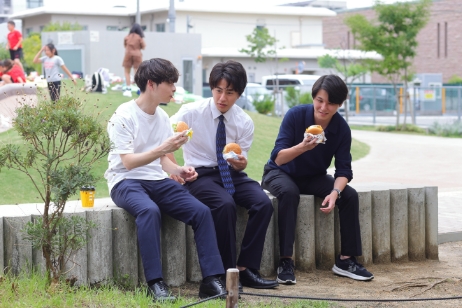 公園でハンバーガーを食べながら談笑している3人